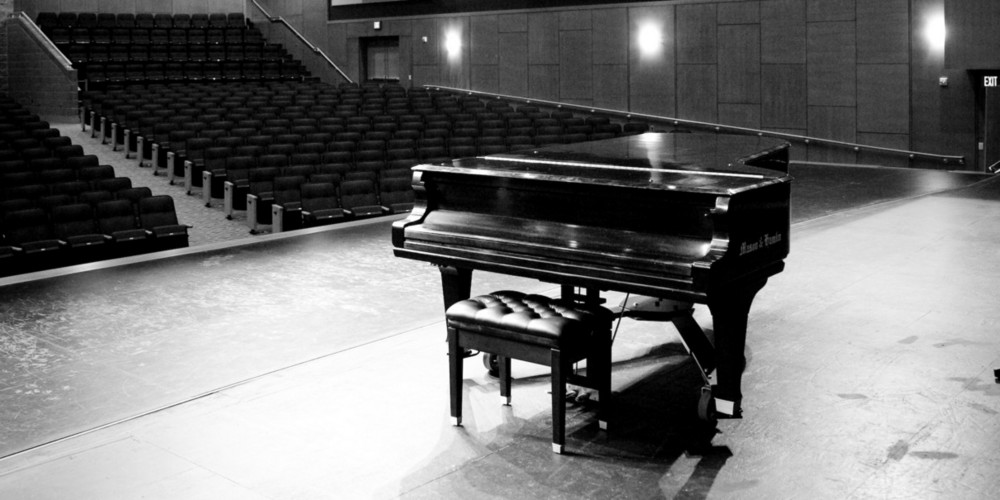 Black and white photo of concert grand piano on stage at OAC